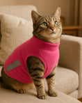 Load image into Gallery viewer, Tabby cat wearing a pink fleece vest with cutouts, sitting on a beige couch in a living room.